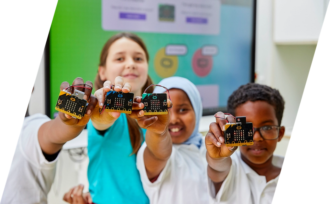 Crianças sorrindo e segurando micro:bits em sala de aula